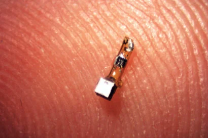 Actual neural-dust mote with piezoelectric crystal and two-contact flexible circuit, on a fingertip.