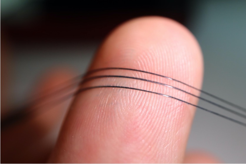Three NeuroString strands stretched across a fingertip.