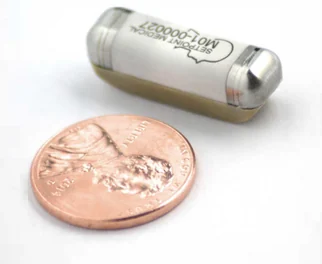 A miniature SetPoint neurostimulator beside a copper coin; its metal capsule and integrated contacts are visible.