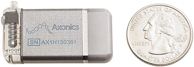 A small Axonics implanted pulse generator beside a U.S. quarter for scale, with its transparent connector header visible.