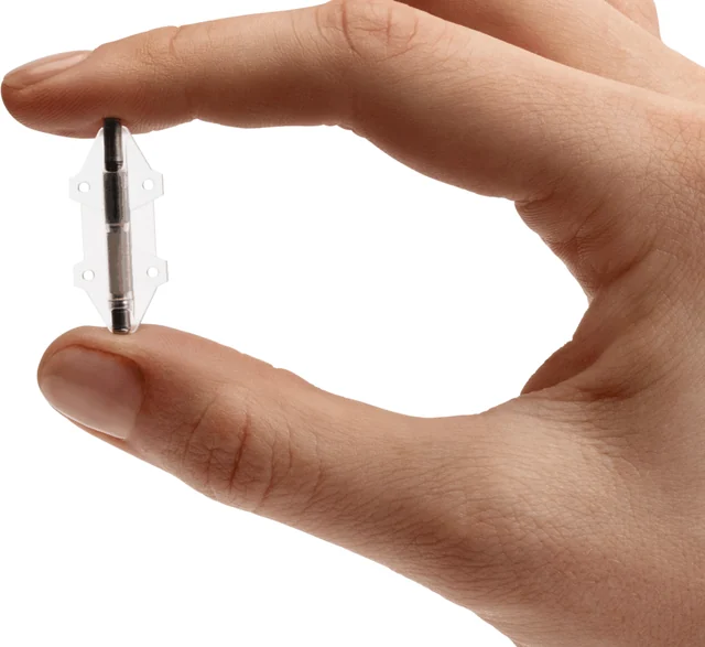 Small cylindrical Revi tibial implant with transparent lateral fixation wings held between two fingertips.
