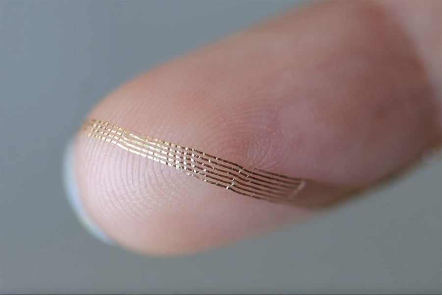 Close photograph of a soft golden Axoft neural probe draped over a fingertip, with parallel traces and multiple rows of electrode sites visible.